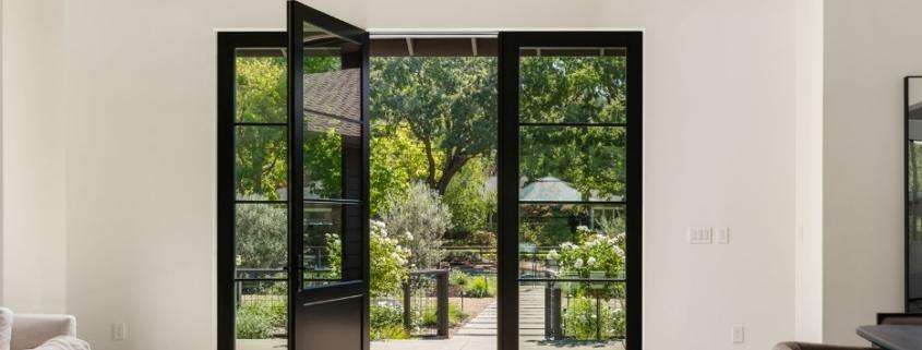 Open black framed glass doors leading from a living room to a garden patio Los Angeles