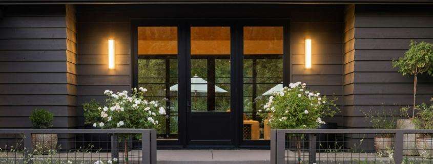 Modern house entrance with black double doors, wall lights, and flower planters in Orange County