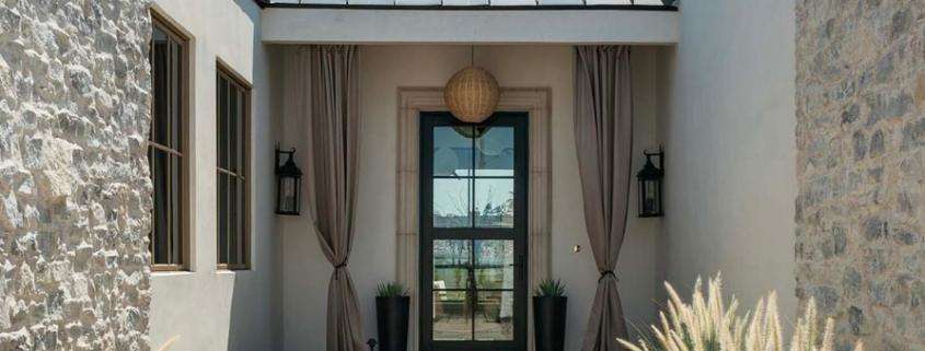 Covered entryway with a glass front door, stone walls, and decorative plants in Yorba Linda